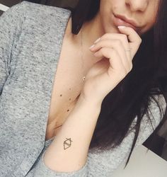 a woman with a small diamond tattoo on her left arm and right hand near her face