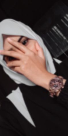 a woman wearing a hijab covers her face with her hand while looking at the camera