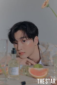 a young man sitting at a table next to a bottle of watermelon and an orange