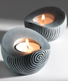 two lit candles sitting on top of a white table next to each other with swirl designs