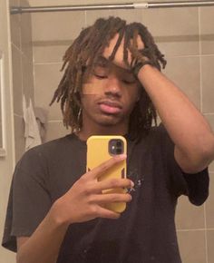 a man with dreadlocks is taking a selfie in the bathroom while holding his cell phone