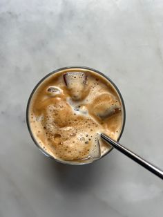 a glass filled with liquid on top of a white counter next to a metal spoon