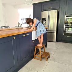 a woman is standing on a stool in the middle of a kitchen with blue cabinets