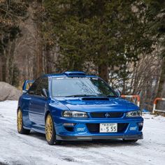 a blue car parked in the snow next to some trees