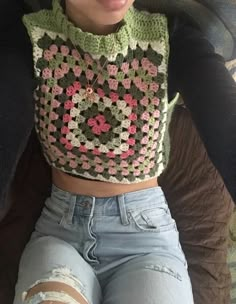 a woman wearing ripped jeans and a crocheted crop top sitting on a couch