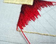 a close up of a piece of cloth with red thread on it and a needle in the middle