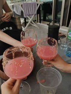 three people are holding up wine glasses with pink liquid in them on a table outside