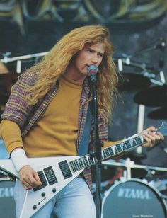 a man with long hair playing an electric guitar at a music festival in front of a microphone