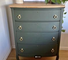 a green dresser with gold handles and knobs on the bottom drawer, next to a potted plant