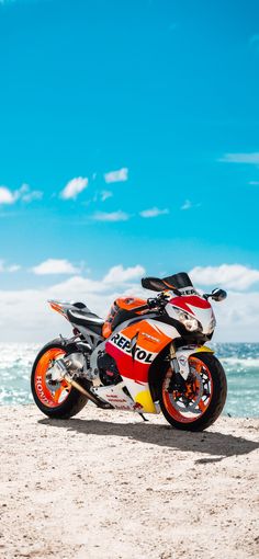 the motorcycle is parked on the beach near the water's edge and blue sky