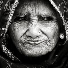 an old woman with wrinkles on her face and headdress is looking at the camera