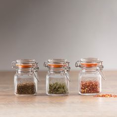 three glass jars filled with spices sitting on top of a wooden table next to each other