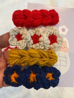 four crocheted hair clips in different colors and sizes are held up by someone's hand