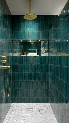 a green tiled bathroom with gold fixtures and blue tiles on the shower wall, along with an open shelf