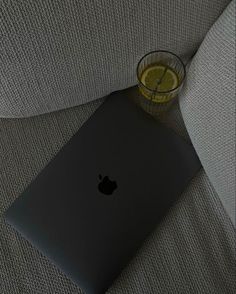 an apple laptop sitting on top of a couch next to a glass of lemonade