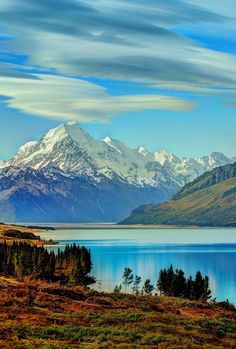 the mountains are covered in snow and have blue skies above them, as well as some water