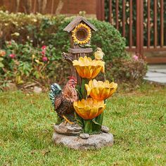 a birdhouse and flowers are in the yard with a rooster statue next to it