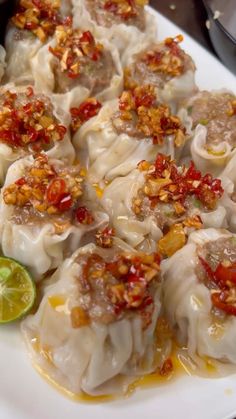 a plate full of dumplings with sauce and garnishes on them next to some lime wedges