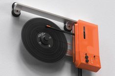 an orange tape dispenser attached to a white wall next to a black cord