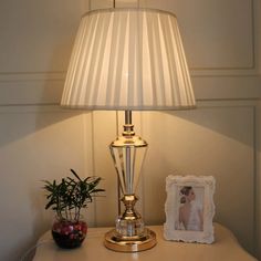 a lamp sitting on top of a white table next to a potted plant and framed photograph