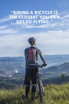 a man standing on top of a lush green field next to a mountain with a bike