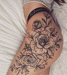 a woman's thigh with flowers and leaves tattooed on her leg, in black ink