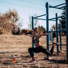 a woman is doing squats in front of a metal structure with an orange bottle