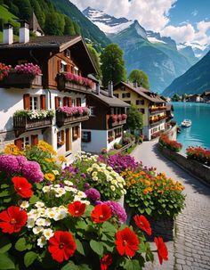 colorful flowers line the side of houses along a river with mountains in the back ground