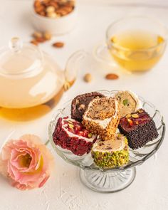 a glass bowl filled with assorted desserts next to a teapot and flower