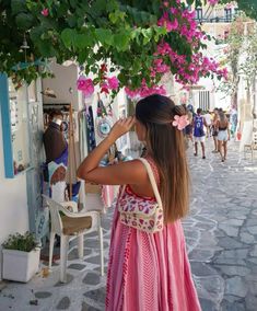 a girl in a pink dress is looking at her cell phone while walking down the street