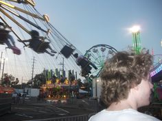 a young man standing in front of a carnival ride at an amusement park during the day