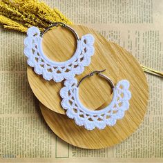 two white crocheted hoop earrings on top of a wooden plate