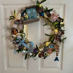 a wreath made out of seashells with a house on the top and lights in the bottom