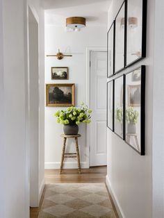 a white hallway with pictures on the wall and flowers in a vase next to it