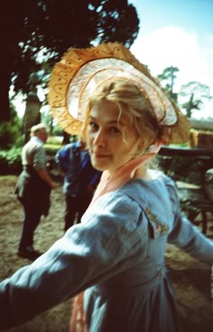 a woman in a blue dress and hat is holding her hand out to the side