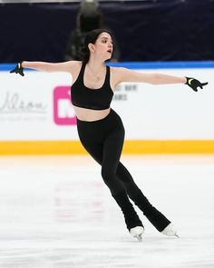 a woman skating on an ice rink in a black top and leggings with her arms outstretched