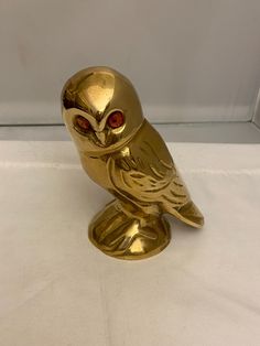 a gold owl figurine with red eyes sitting on a white tableclothed surface