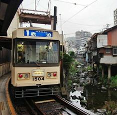 a train traveling down tracks next to buildings and a river in the middle of town