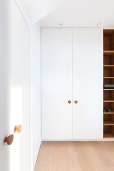 an empty room with white cabinets and wood flooring on the walls, along with wooden shelves