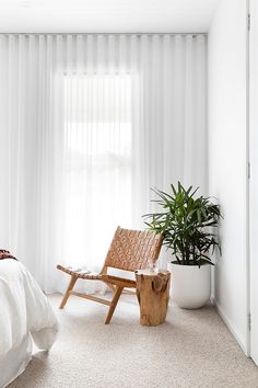 a white bedroom with a wooden chair and potted plant