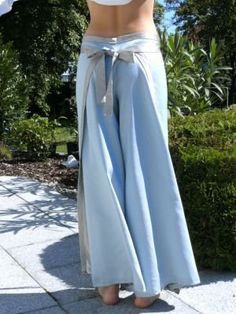 a woman wearing blue pants and a white top is standing in front of some bushes