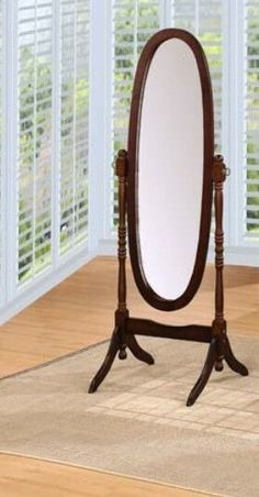 an oval mirror sitting on top of a wooden stand in front of a white window