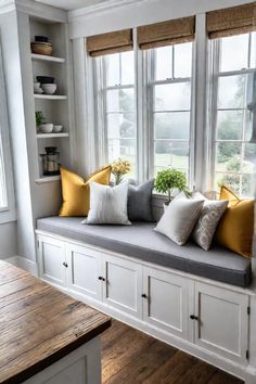 a window seat with yellow and gray pillows on it in front of a wooden table