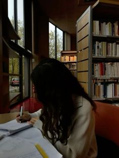 a woman sitting at a table in front of a book shelf filled with books and papers