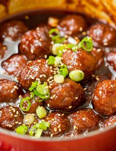 a red bowl filled with meatballs covered in sauce and garnished with green onions