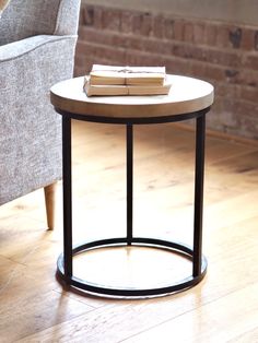 a round table with books on it in front of a chair and brick wall behind it