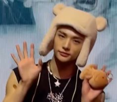 a young man wearing a hat and holding a teddy bear in front of his face