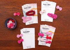 pink and red hair clips sitting on top of a wooden table next to some paper