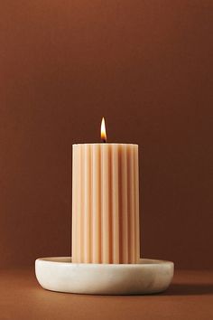 a lit candle sitting on top of a white plate in front of a brown background