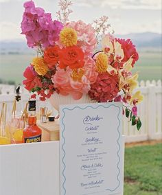 a table with flowers and drinks on it in front of a fenced in area